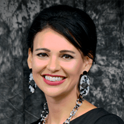 Smiling woman with dark hair and with earrings, necklace and black blouse.